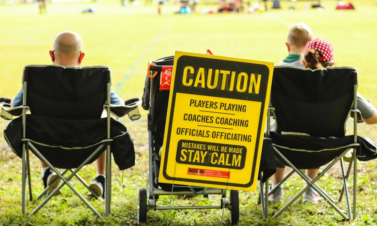 Stock image of youth sports parents in front of a caution sign warning of poor spectator behavior