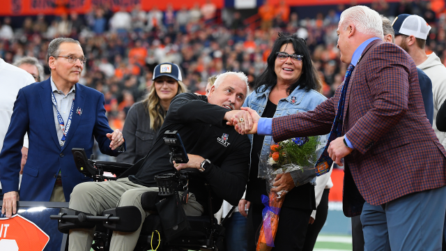 Seated in a motorized wheelchair, Paul Gait shakes Gary Gait's hand during his jersey retirement ceremony at Syracuse's JMA Wireless Dome