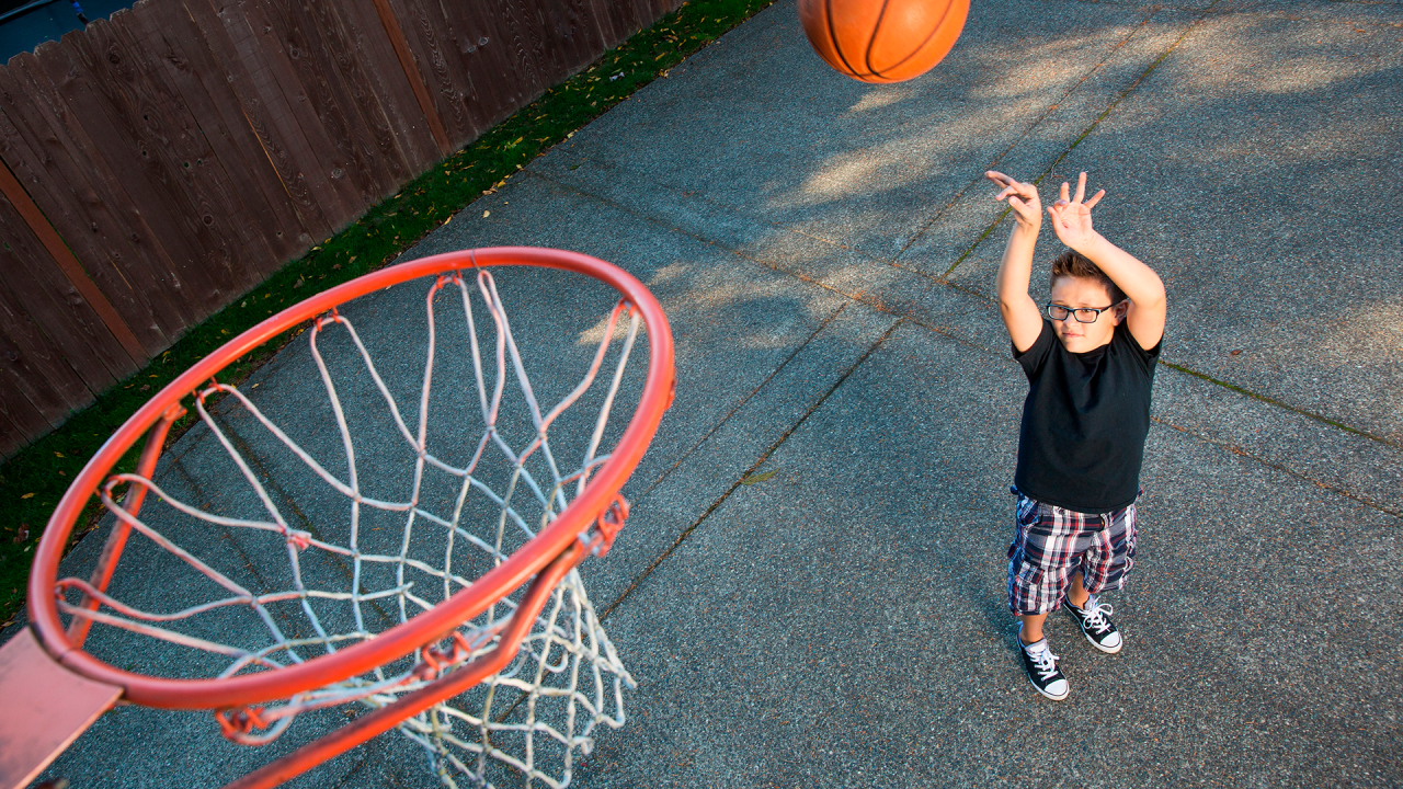 Boy shooting a basketball toward a hoop in his driveway